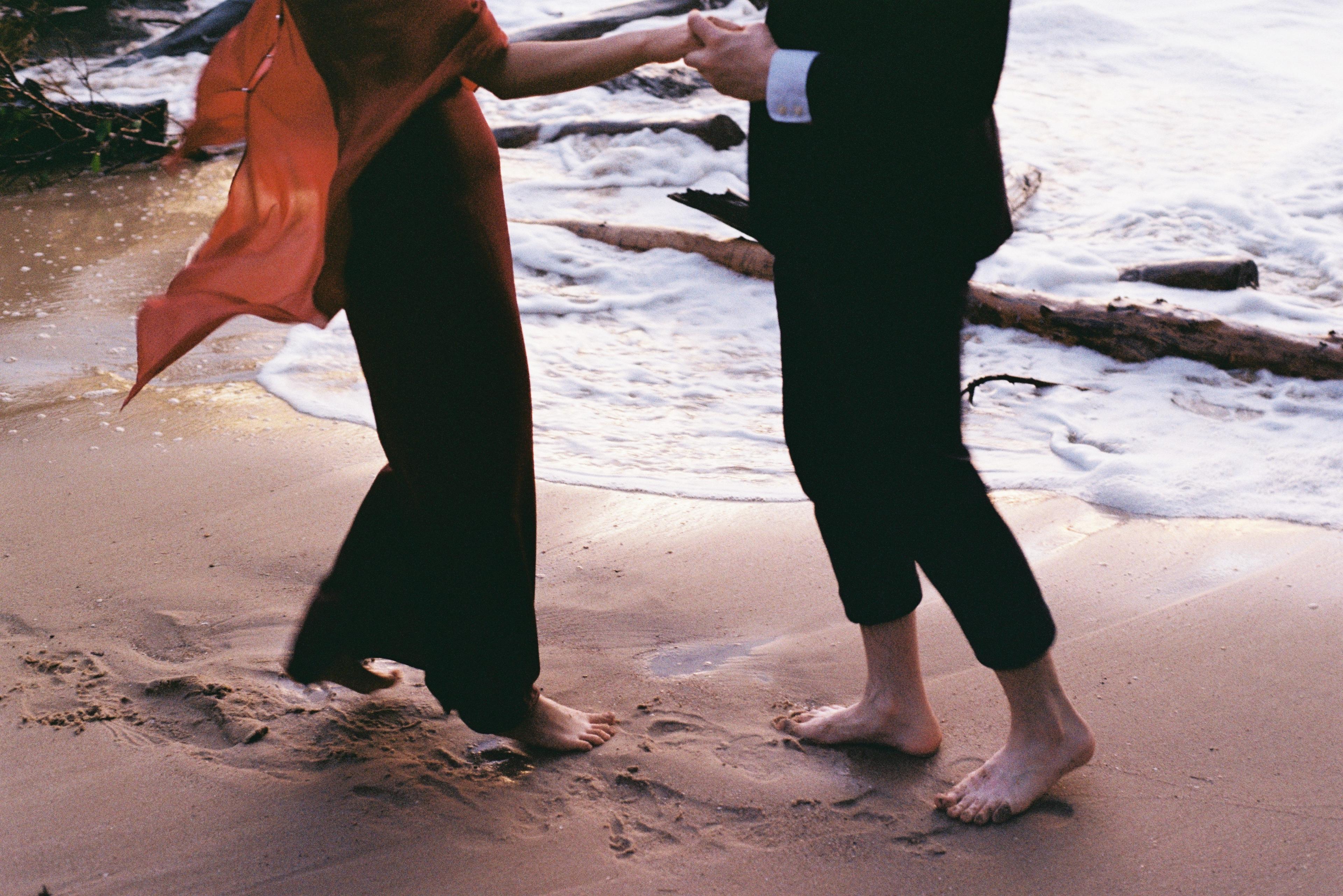 A couple walking barefoot along the shore at sunset