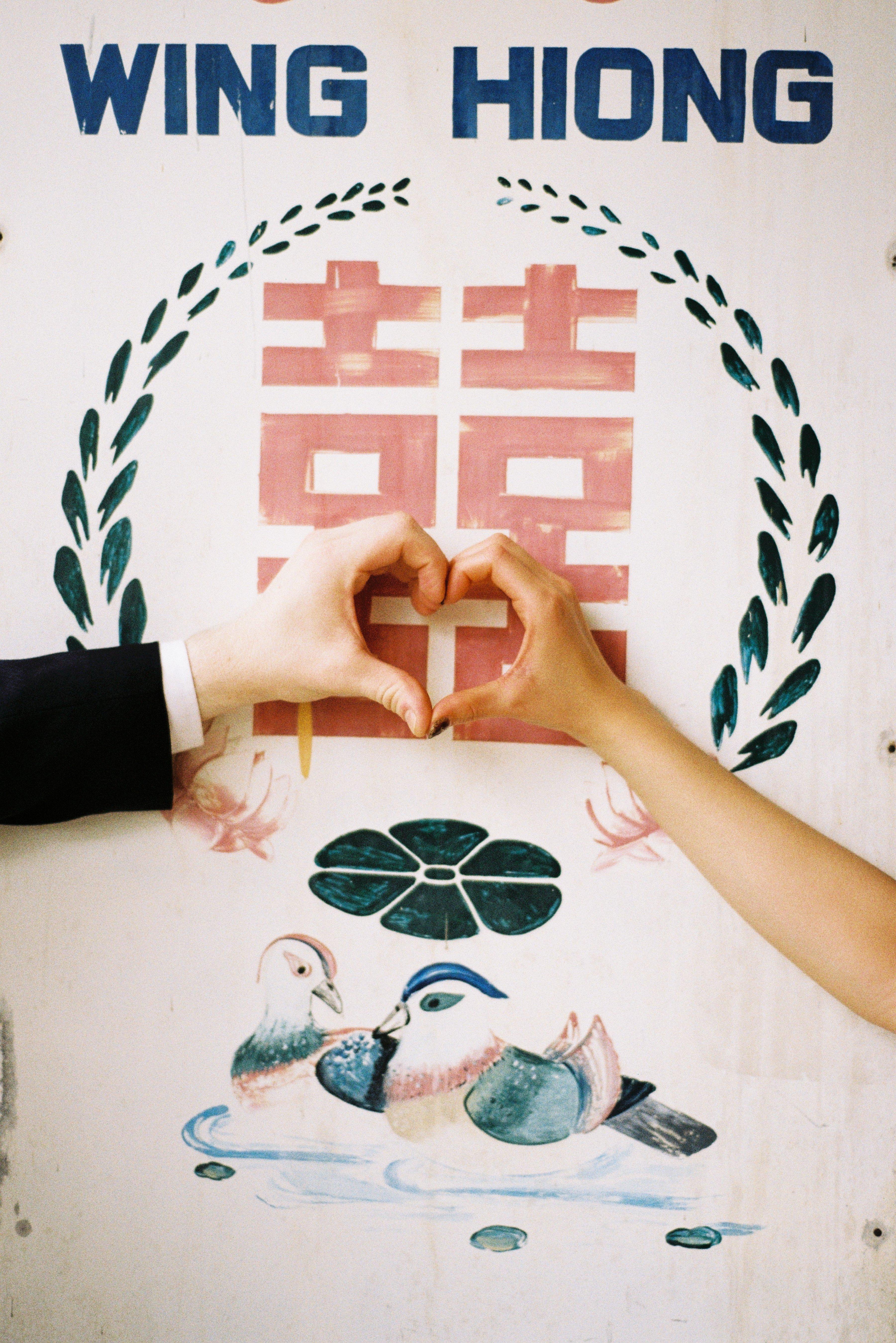 Hands forming a heart over a hand-painted double happiness sign