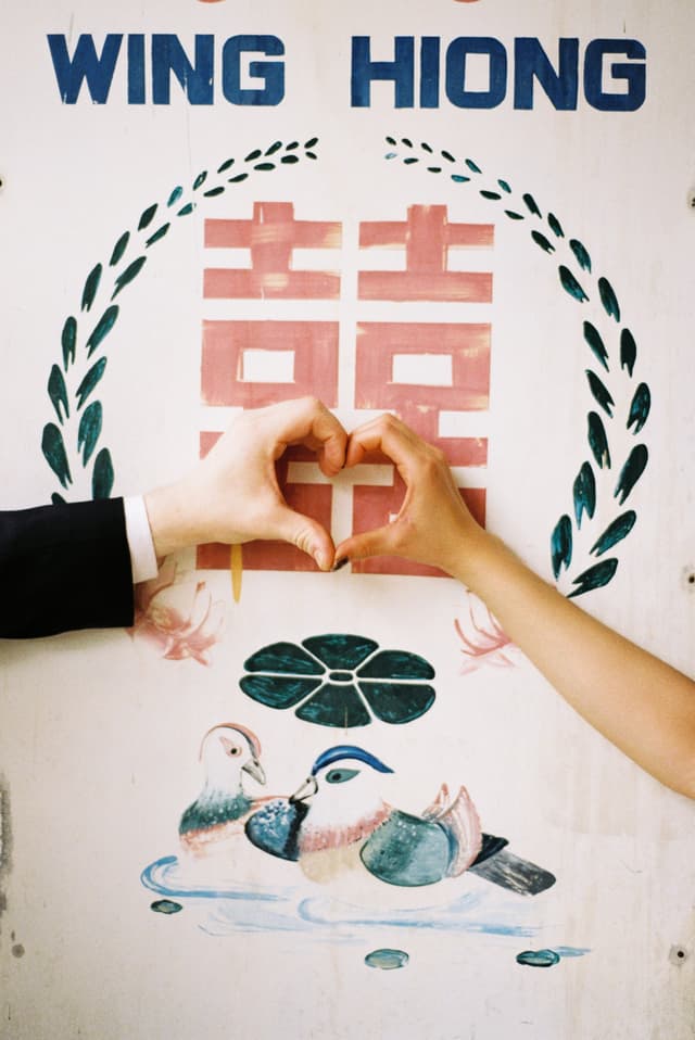 Hands forming a heart over a hand-painted double happiness sign